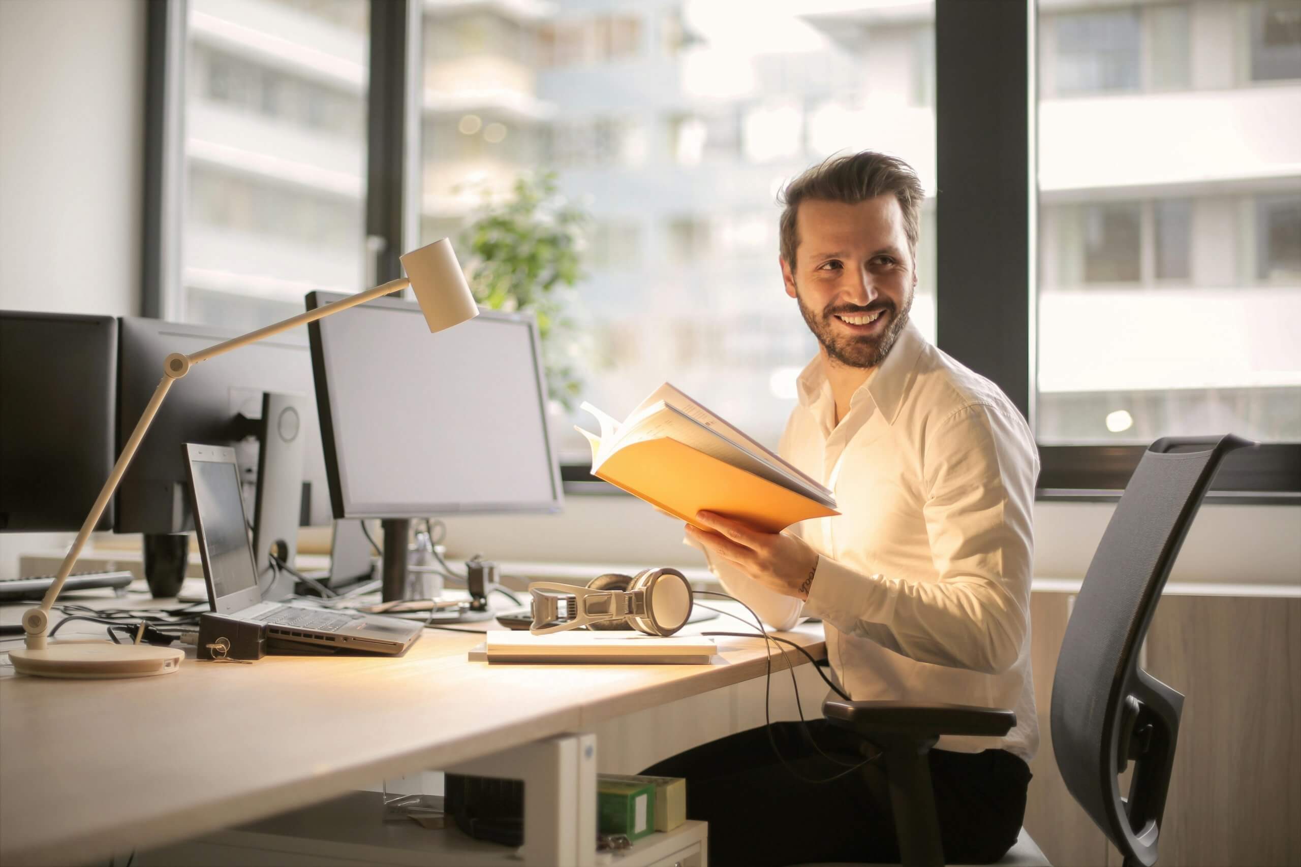 Homme souriant assis à son bureau ergonomique, lisant un dossier au travail — illustration de la prévention des TMS en entreprise.