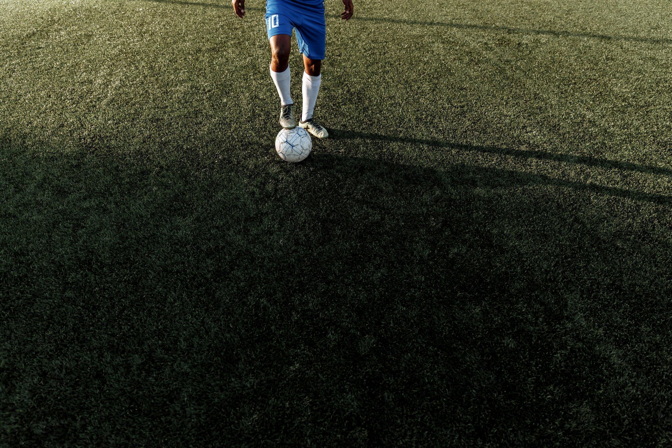 Joueur de football en tenue bleue dribblant un ballon sur un terrain synthétique, illustrant la préparation mentale pour améliorer les performances sportives.
