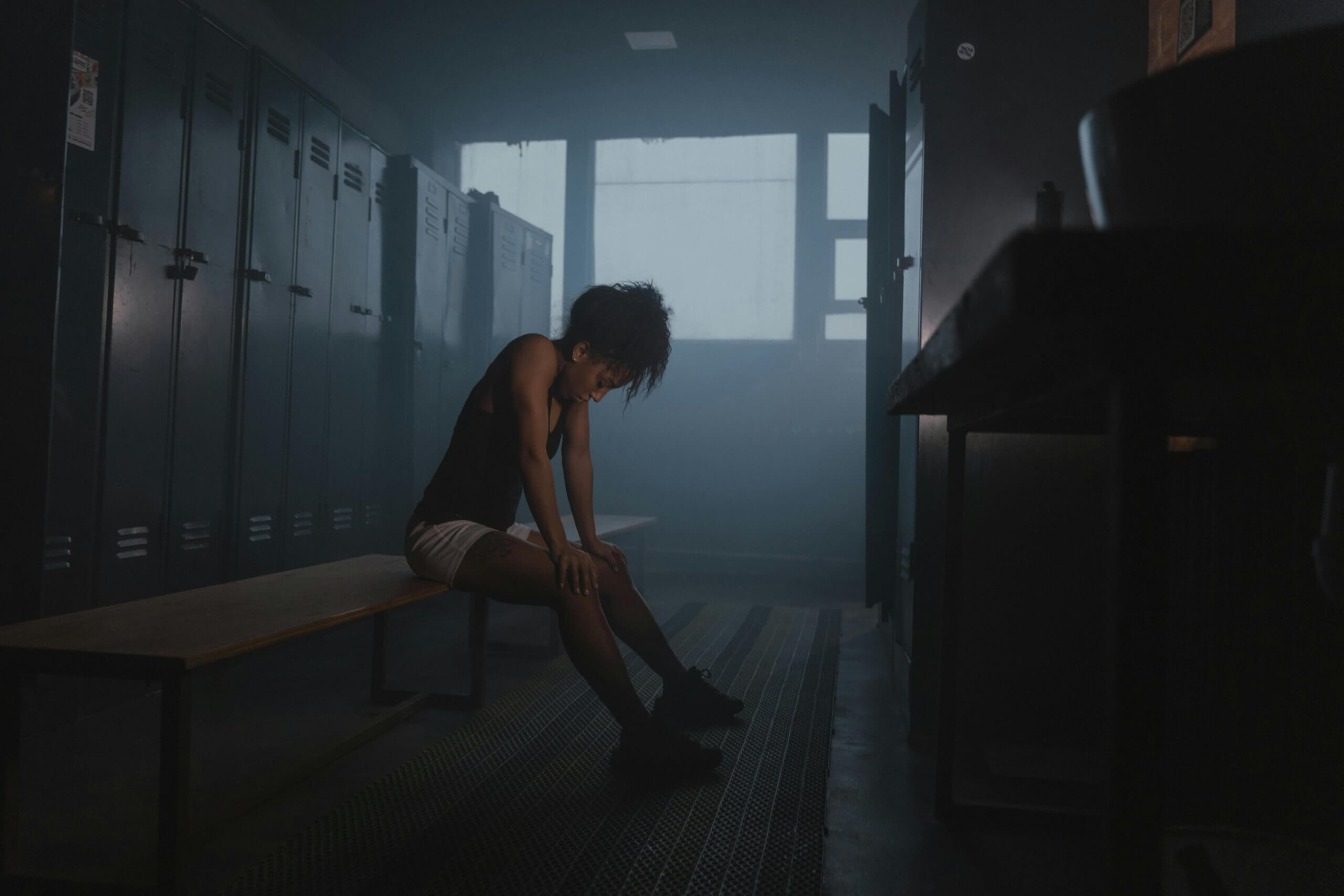 Sportive assise dans un vestiaire, tête baissée, illustrant un manque de concentration ou un moment de doute avant une performance sportive, symbole des enjeux mentaux dans le sport.